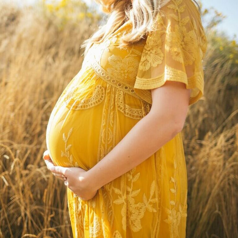 Femme enceinte en robe jaune caressant son ventre, bienfaits de la réflexologie plantaire pendant la grossesse