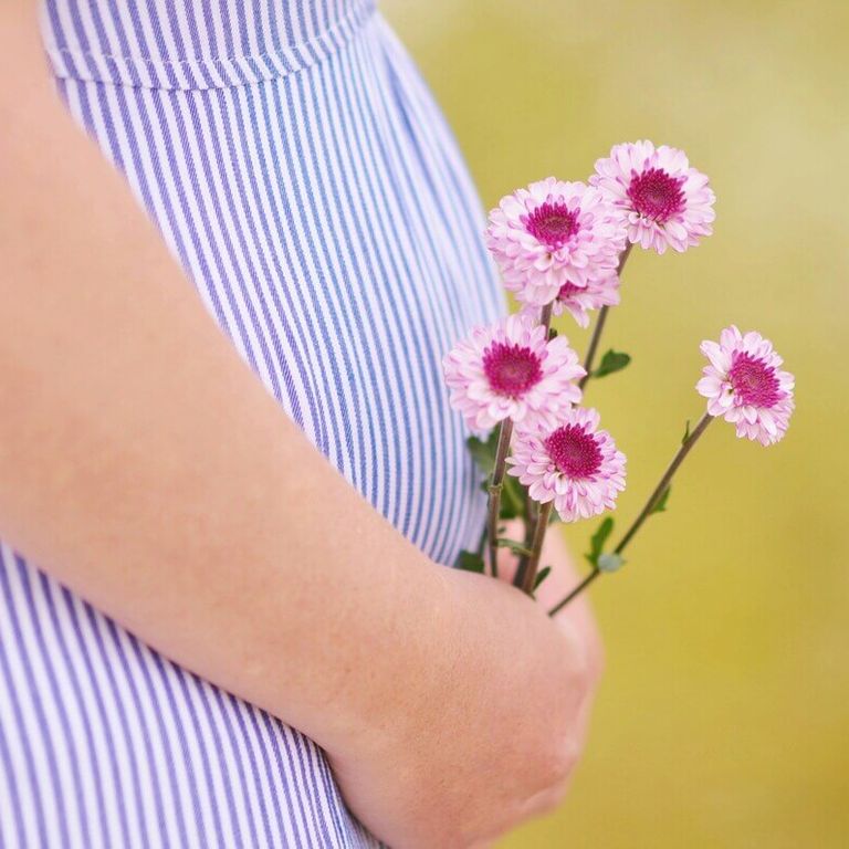Femme enceinte tenant des fleurs roses, pour préparer sa grossesse naturellement avec la réflexologie plantaire